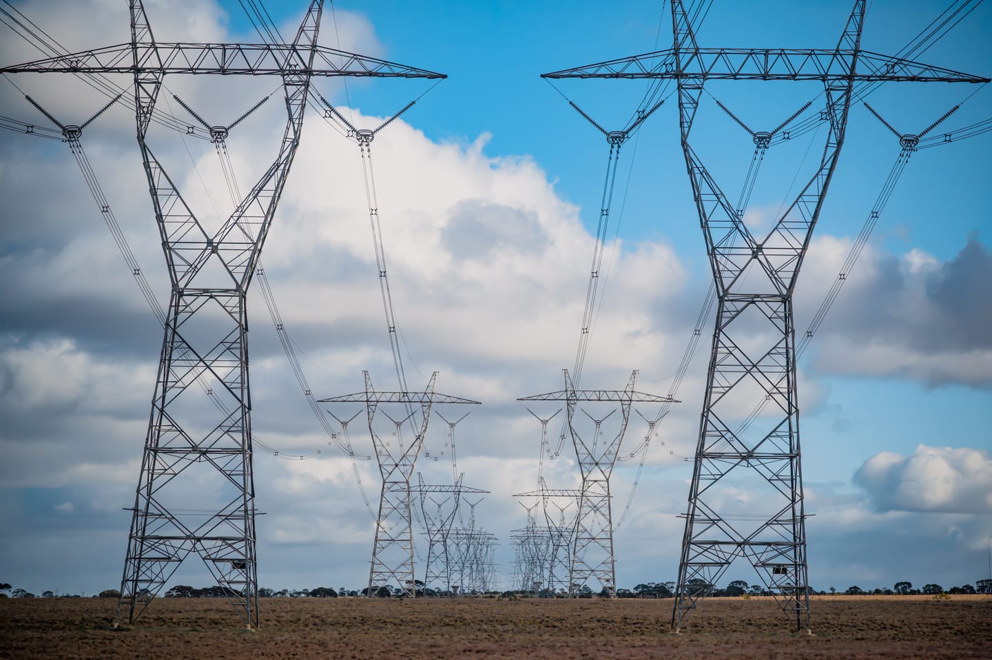 Reihen von Hochspannungsmasten, die unter bewölktem Himmel offenes Ackerland überqueren