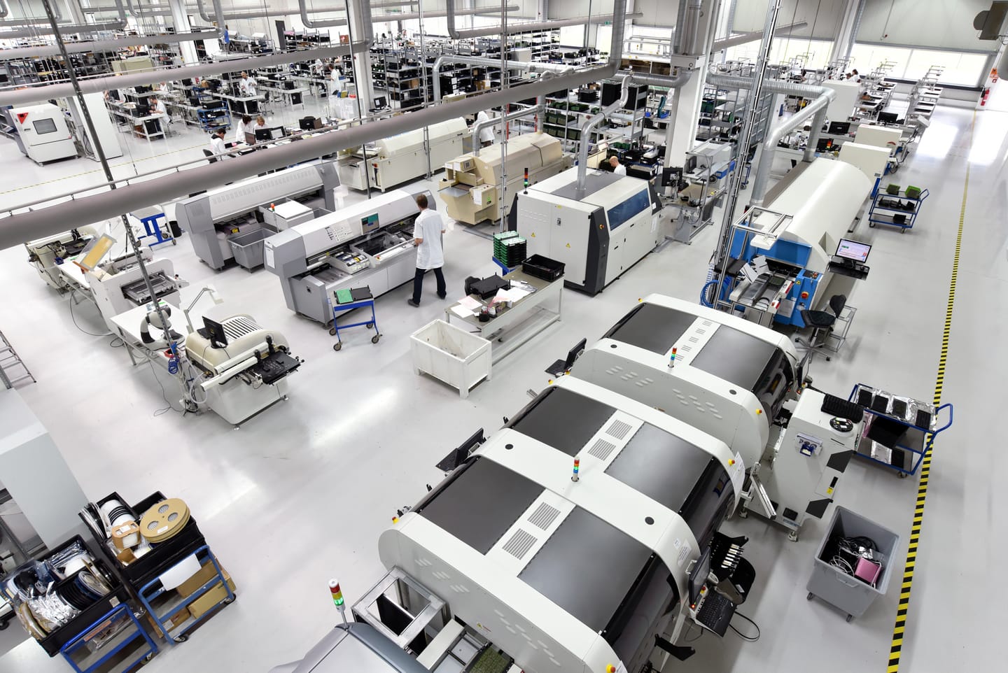 Technikerinnen und Techniker zwischen CNC-Maschinen in einer hellen Elektronikfertigungshalle