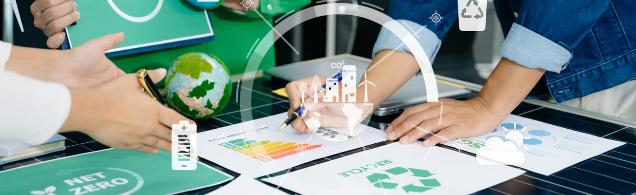 Several people around a table reviewing printed energy ratings, recycling and net zero documents beside a small globe